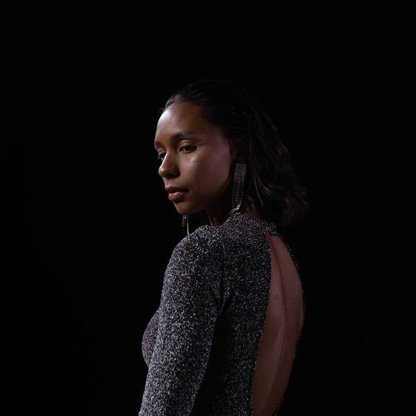 Woman performing a calm balancing yoga pose in a dark studio.